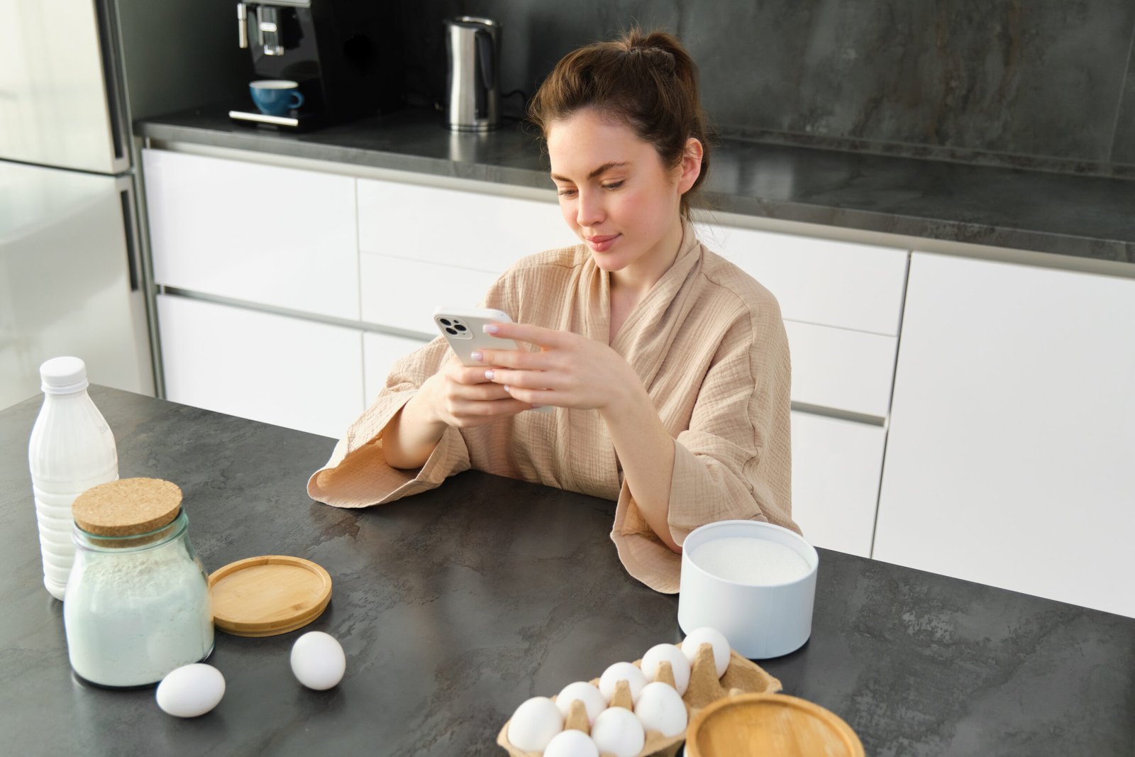 Attractive young cheerful girl baking at the kitchen, making dough, holding recipe book, having ideas